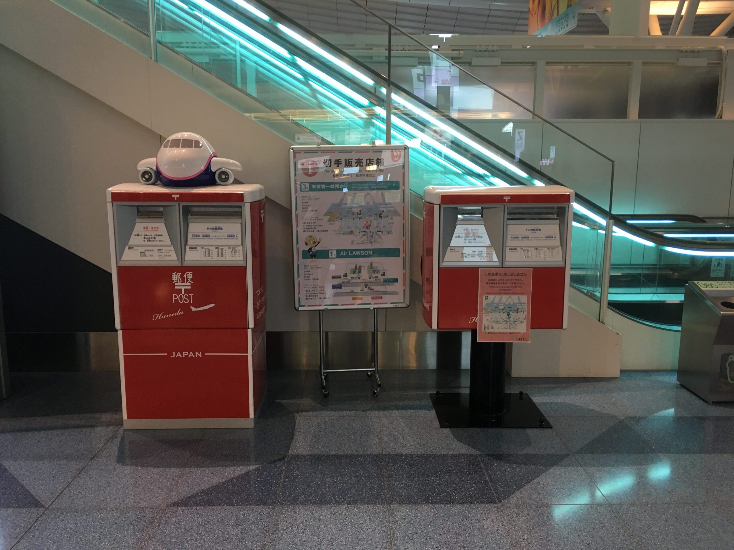 Haneda Airport red post boxes and stamp-shop map near the escalator.
