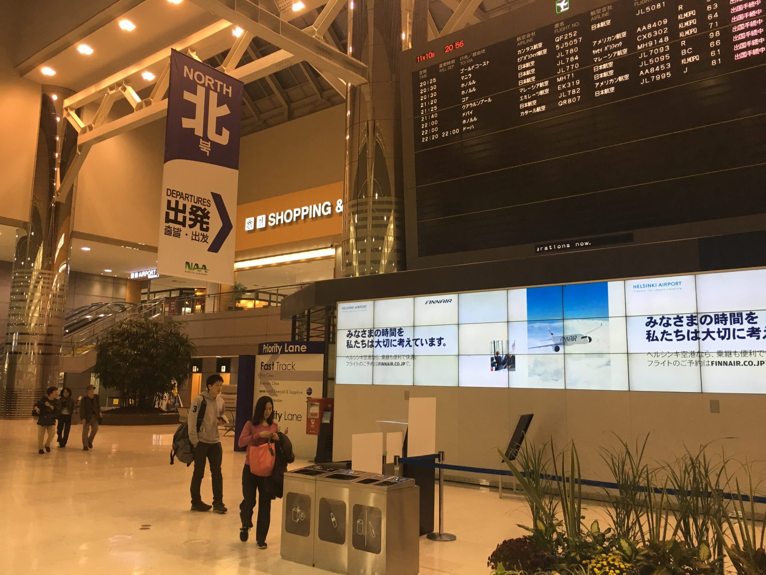 Narita Airport Terminal 2 North departures area with travelers and flight information displays.