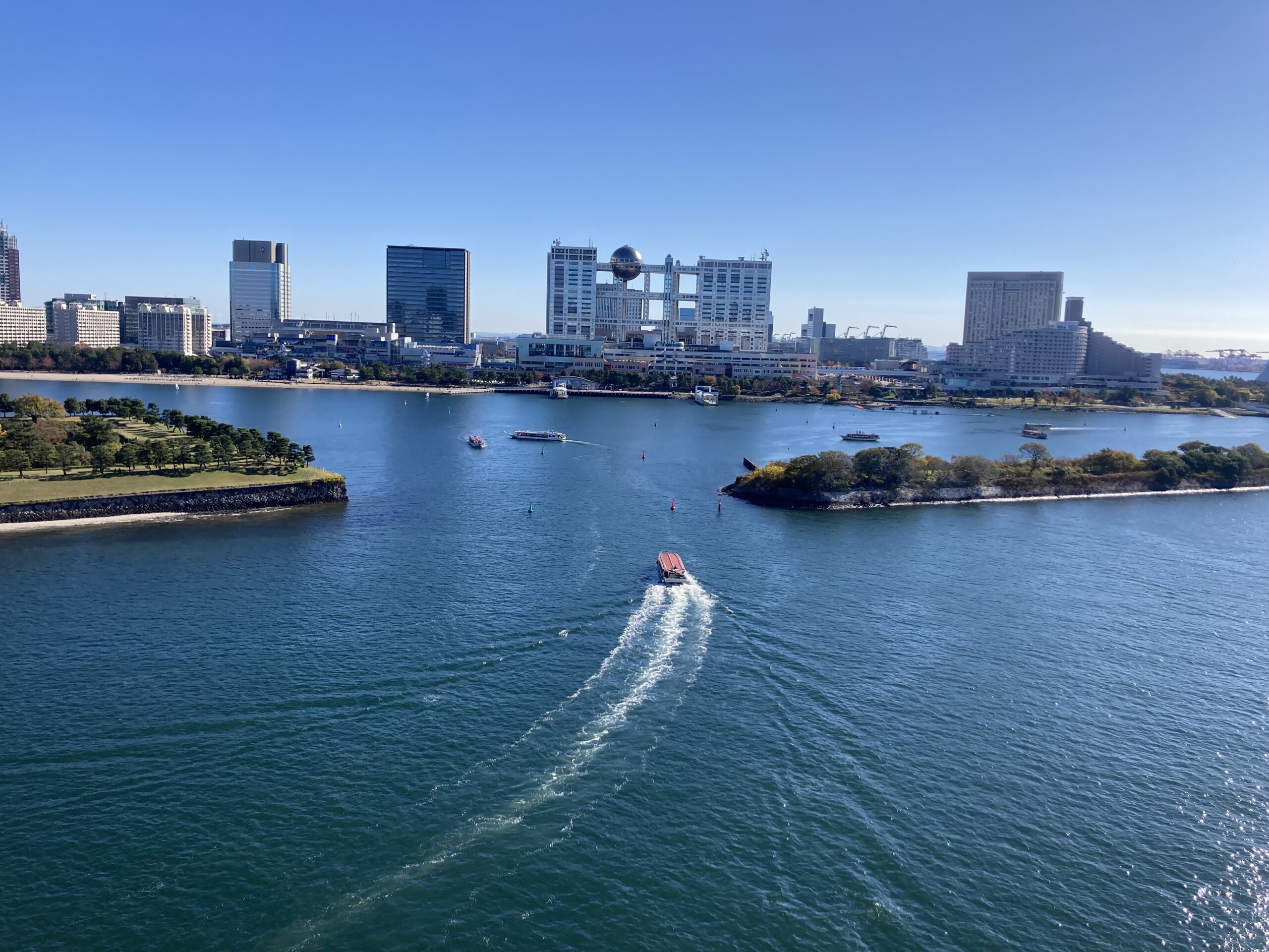 View of Tokyo Bay and Odaiba skyline from Rainbow Bridge with boats on the water.